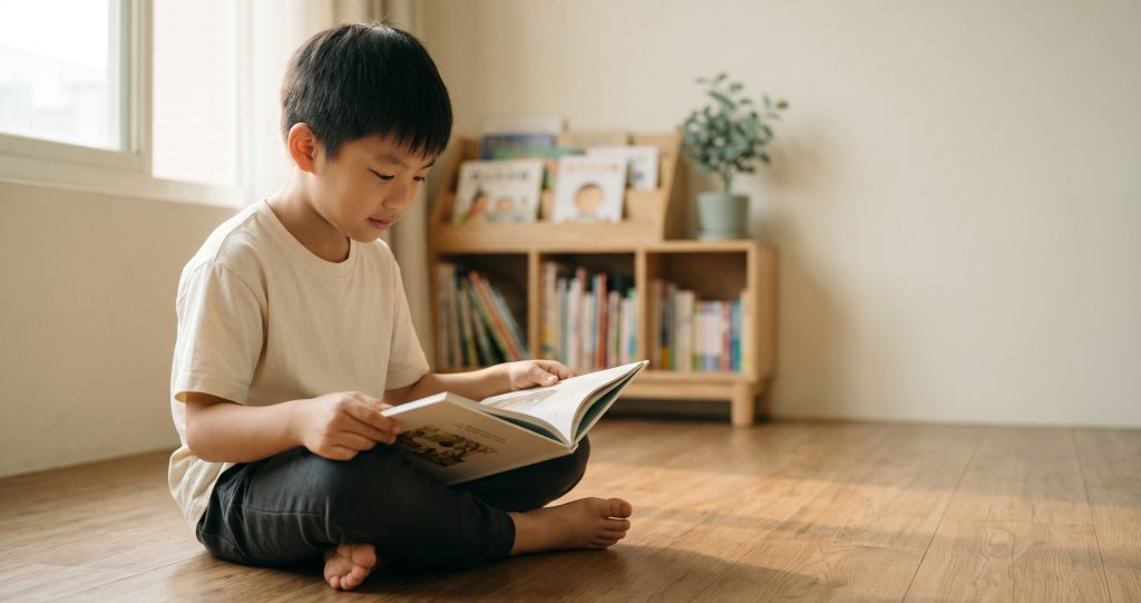 小二男孩坐在家中地板上安靜閱讀橋樑書，呈現情緒穩定與專注力訓練後的改變