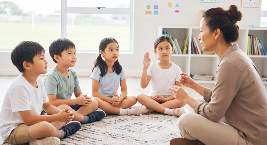 孩子們圍坐在教室地墊上專注聽老師引導，一名孩子舉手回應，呈現運動訓練陪伴下情緒穩定、能安坐參與並自我控制的樣子