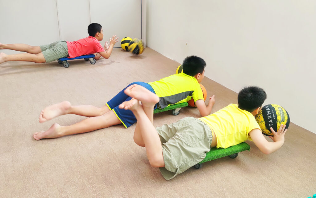三位國小男童趴在滑板上進行核心與平衡協調訓練，提升專注力與動作協調能力