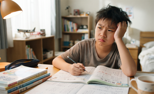 開學前，一名國小男童托腮盯著作業本、遲遲無法動筆，呈現作業拖延與分心的收心困難