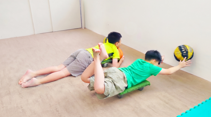 孩子俯臥在滑板車上做核心肌群與姿勢維持練習，屬於前額葉強化運動訓練課程的一環